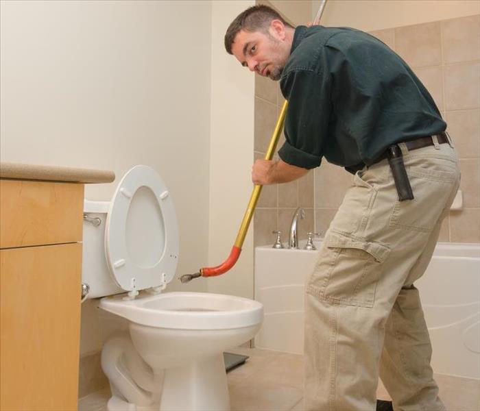 Plumber unclogging a toilet with manual auger