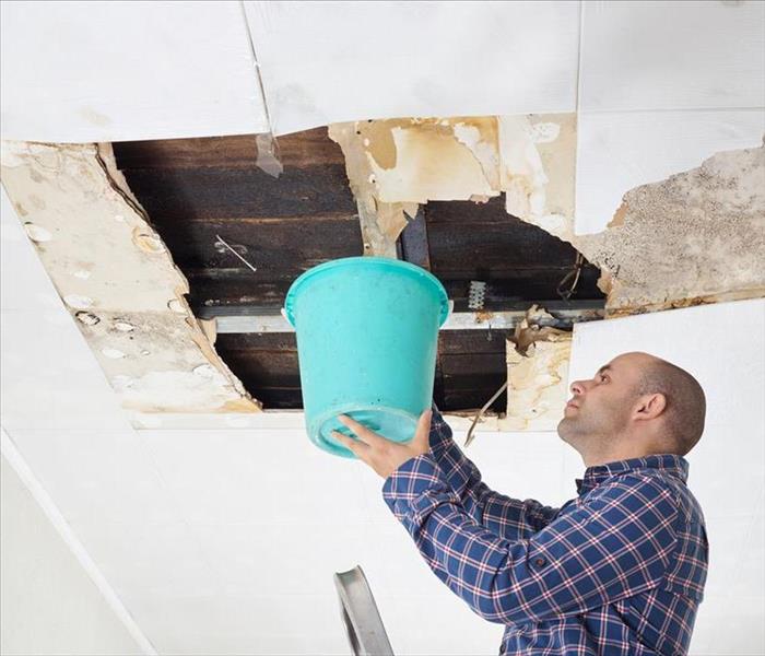 Man holding a bucket toward a leaking a roof